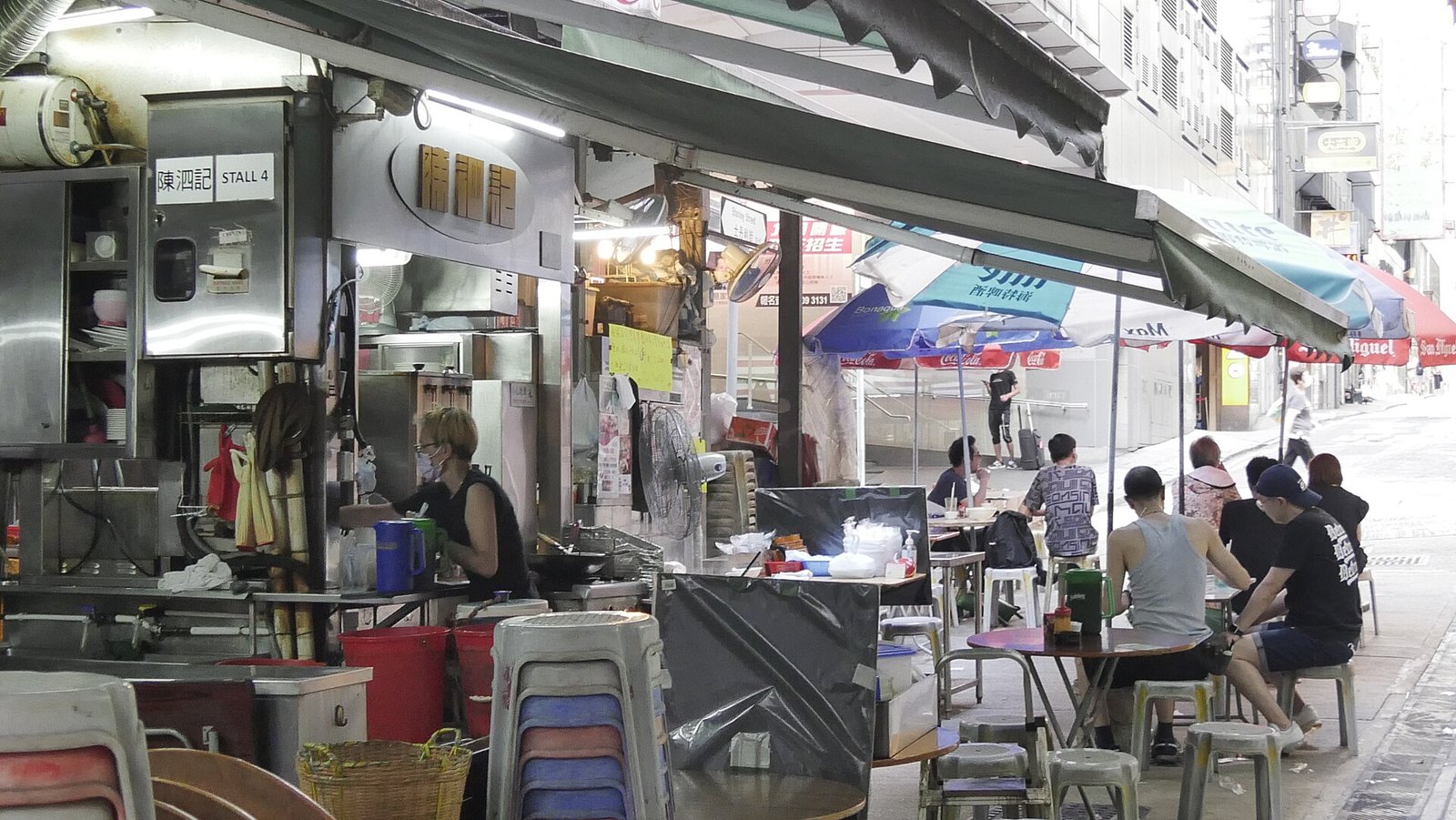 A licensed dai pai dong food stall in Hong Kong with awnings, diners at folding tables and a wok range