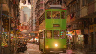 Green double-decker Hong Kong tram on a narrow street at golden hour