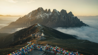 Wutai Shan pilgrimage ridge at sunrise with prayer flags, snowy peaks and a monastery below