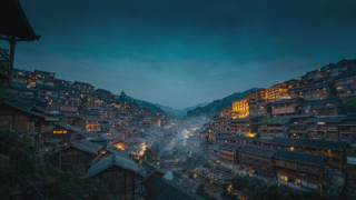 Xijiang Miao Village in Guizhou at dusk with hundreds of lit timber houses on two hillsides