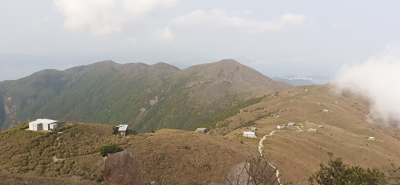 The open ridge and summit path of Sunset Peak, with stone huts and grassland