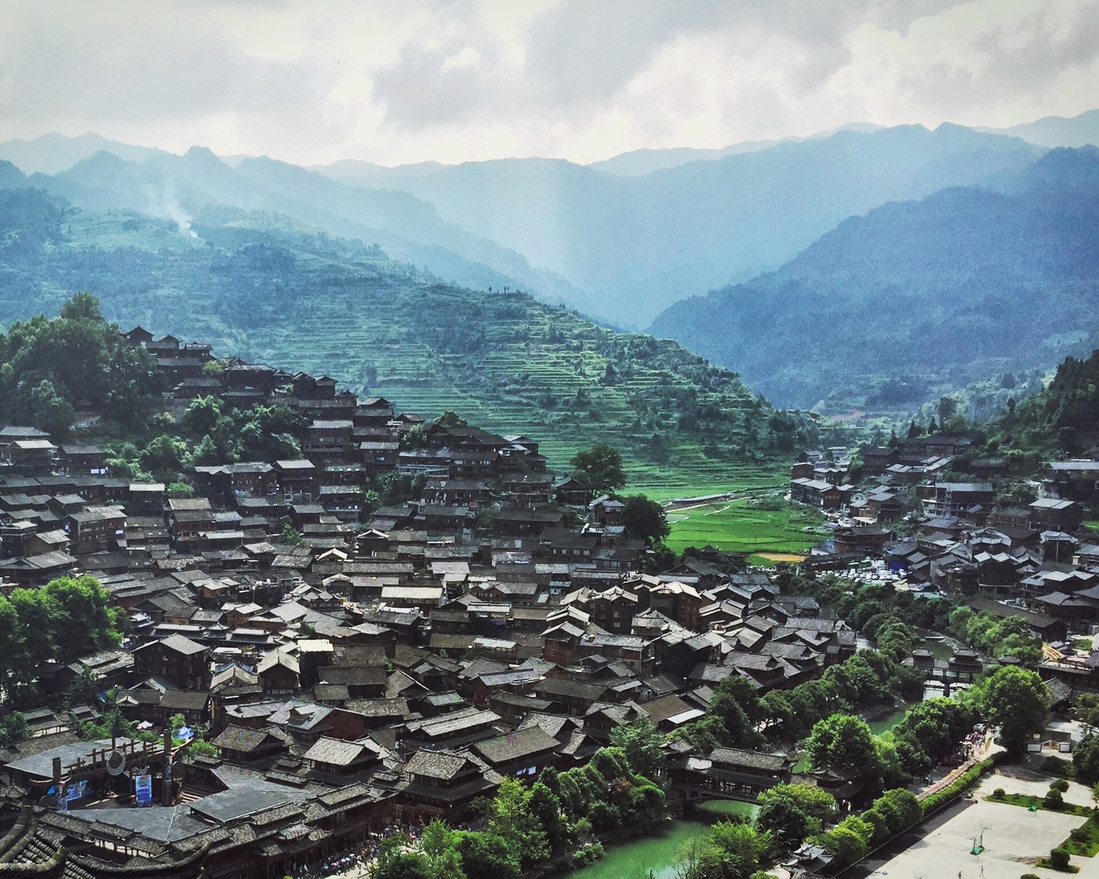 Timber houses of Xijiang Qianhu Miao Village stacked on a hillside above green rice fields